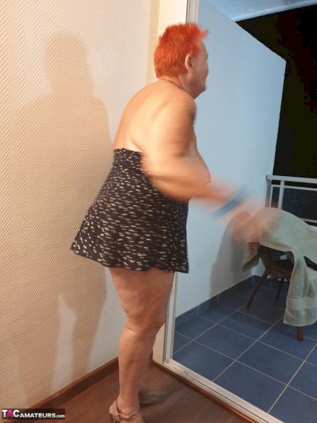 Fat nan with short red hair presses her big boobs and butt up against glass