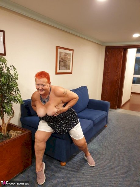 Fat nan with short red hair presses her big boobs and butt up against glass