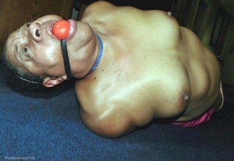 Overweight black woman Trixie struggles against a ball gag while hogtied