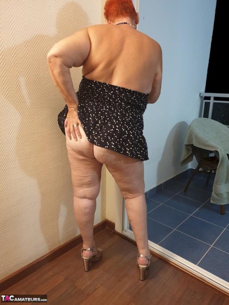 Fat nan with short red hair presses her big boobs and butt up against glass