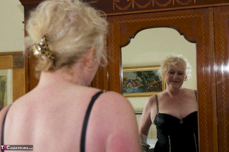 Blonde granny admires herself in a mirror while wearing lingerie and nylons