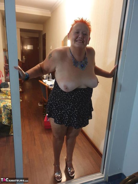 Fat nan with short red hair presses her big boobs and butt up against glass