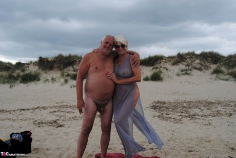 Older platinum blonde Dimonty blows a kiss while at a nude beach with her man