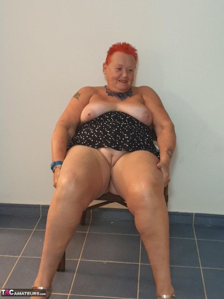 Fat nan with short red hair presses her big boobs and butt up against glass