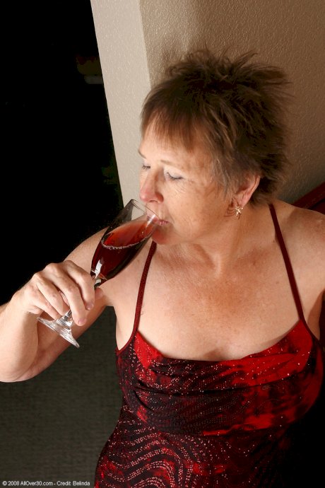 Old granny with big tits Sandra D doffs her red dress and poses nude