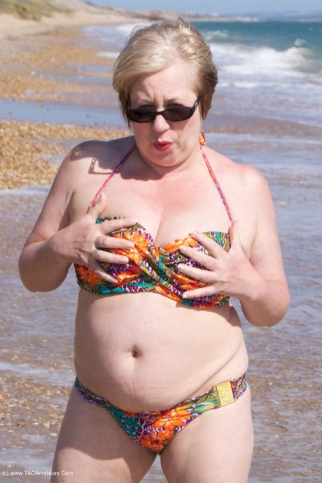 Mature UK woman Speedy Bee wears sunglasses while getting naked at the beach