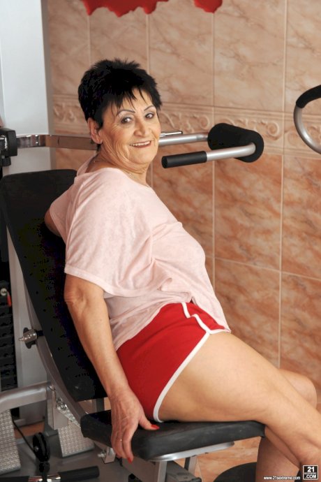 Sassy granny Anastasia strips at the gym to spread naked on the equipment