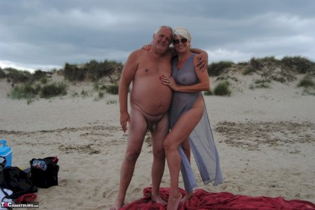 Older platinum blonde Dimonty blows a kiss while at a nude beach with her man