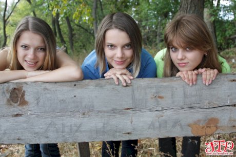 Three young looking girls gets naked on a wooden bench in the countryside