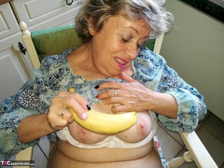 Horny granny Caro sticks a banana inside her natural pussy on kitchen chair