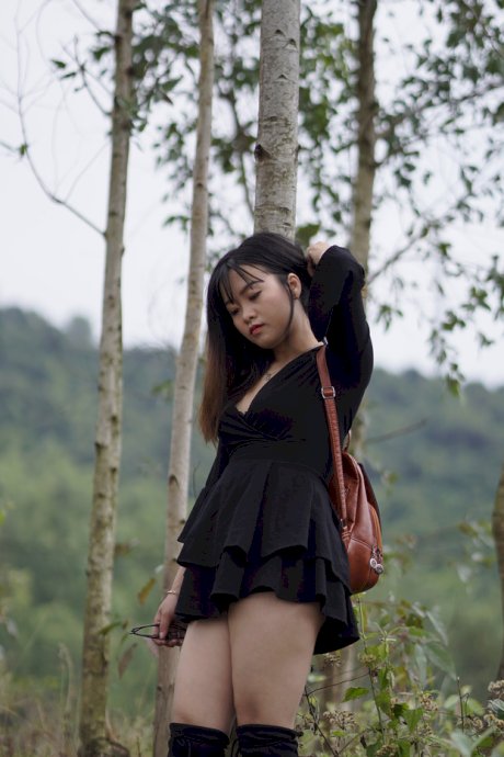 Gorgeous Asian babe posing in her black dress and boots in nature