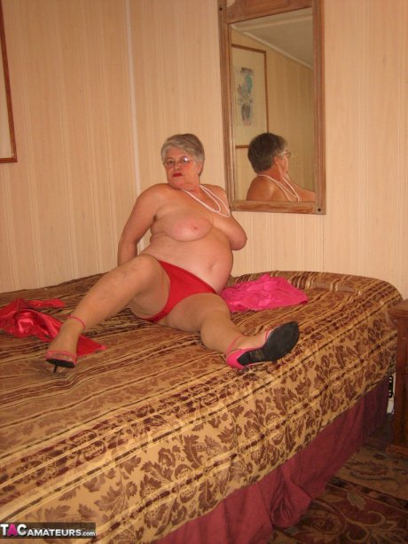 Silver haired nan Girdle Goddess pulls her hose down around her knees on a bed