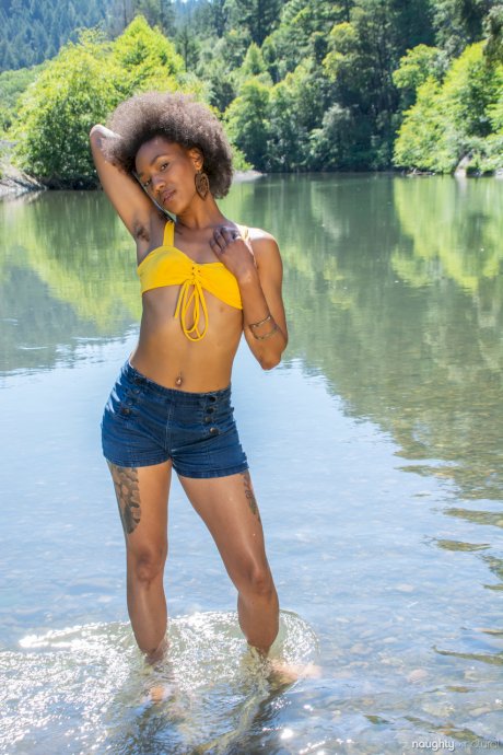 Afro-American babe Nikki Darling exposes her hairy inked body in the river