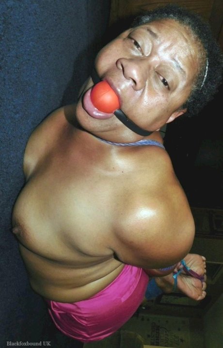 Overweight black woman Trixie struggles against a ball gag while hogtied