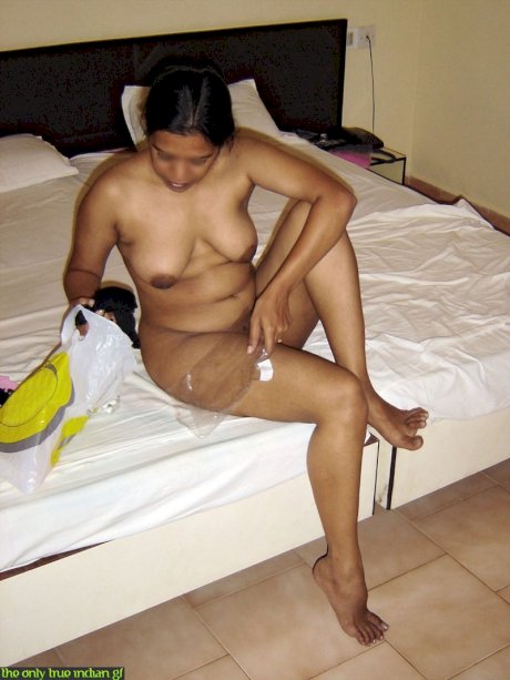 Naked Indian wife pulls on black nylons and garters on edge of bed