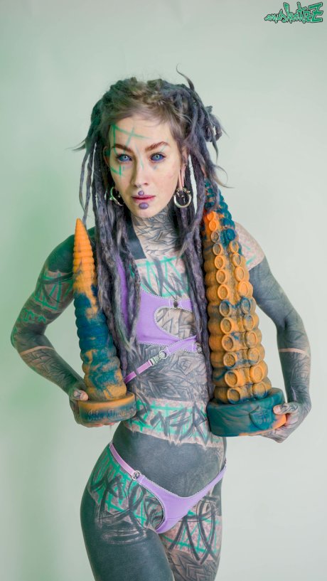 Heavily tattooed girl Anuskatzz holds a couple of taintacle toys in the nude