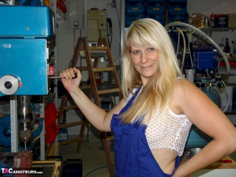 Mature blonde removes her overall before masturbating in workshop