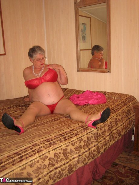 Silver haired nan Girdle Goddess pulls her hose down around her knees on a bed