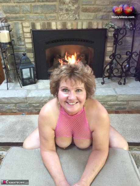 Mature woman Busty Bliss shows her natural tits in front of a fireplace
