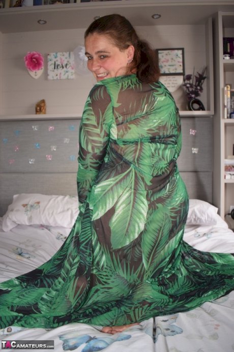 Fat woman exposes herself on a bed while wearing a long dress