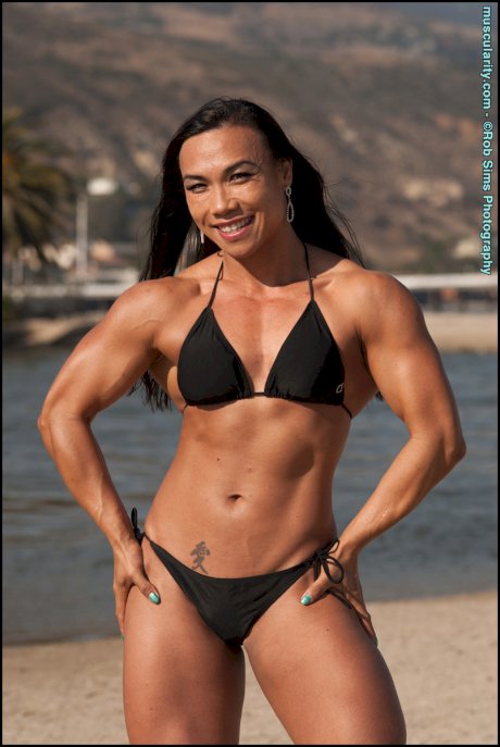 Asian bodybuilder Tram Nguyen flexes upon a beach in a black bikini