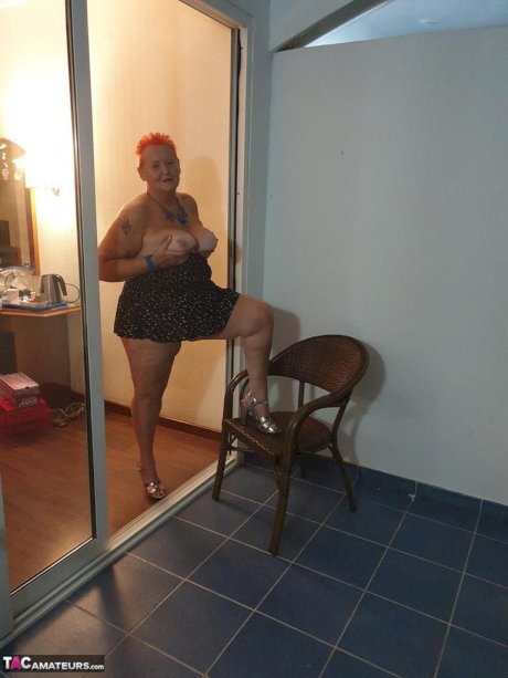 Fat nan with short red hair presses her big boobs and butt up against glass