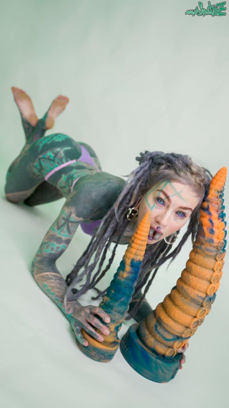Heavily tattooed girl Anuskatzz holds a couple of taintacle toys in the nude